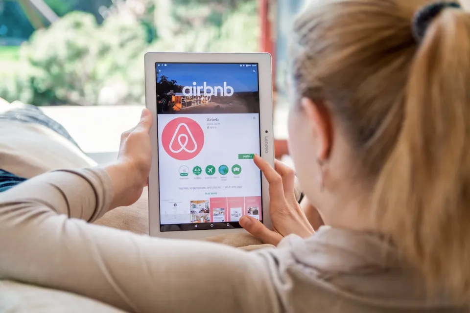 Blonde woman looking for rental on Airbnb app on tablet.